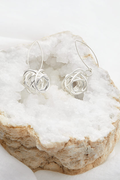 A pair of Silver Squiggle Earrings sitting on a rock, beautifully adorned with beads.