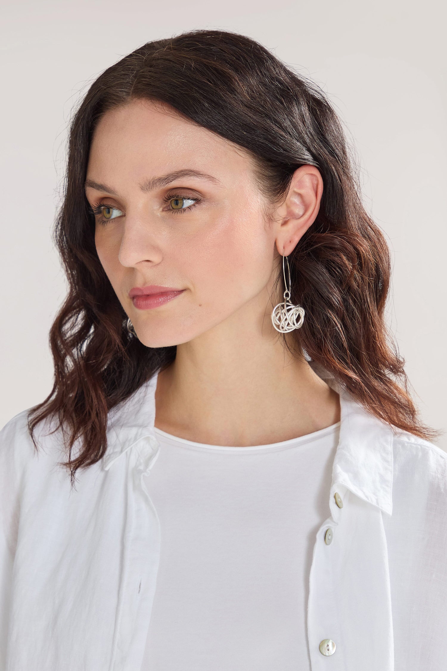 A woman with shoulder-length dark hair, wearing a white shirt and Silver Squiggle Earrings crafted from nickel-free metals, looks forward.