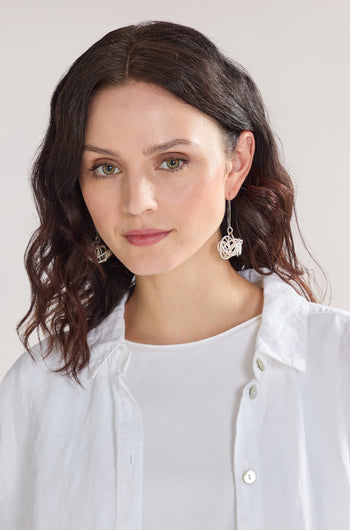 A woman with shoulder-length dark hair is wearing a white shirt and intricate, one-of-a-kind Silver Squiggle Earrings made from nickel-free metals, looking slightly to the side against a plain background.