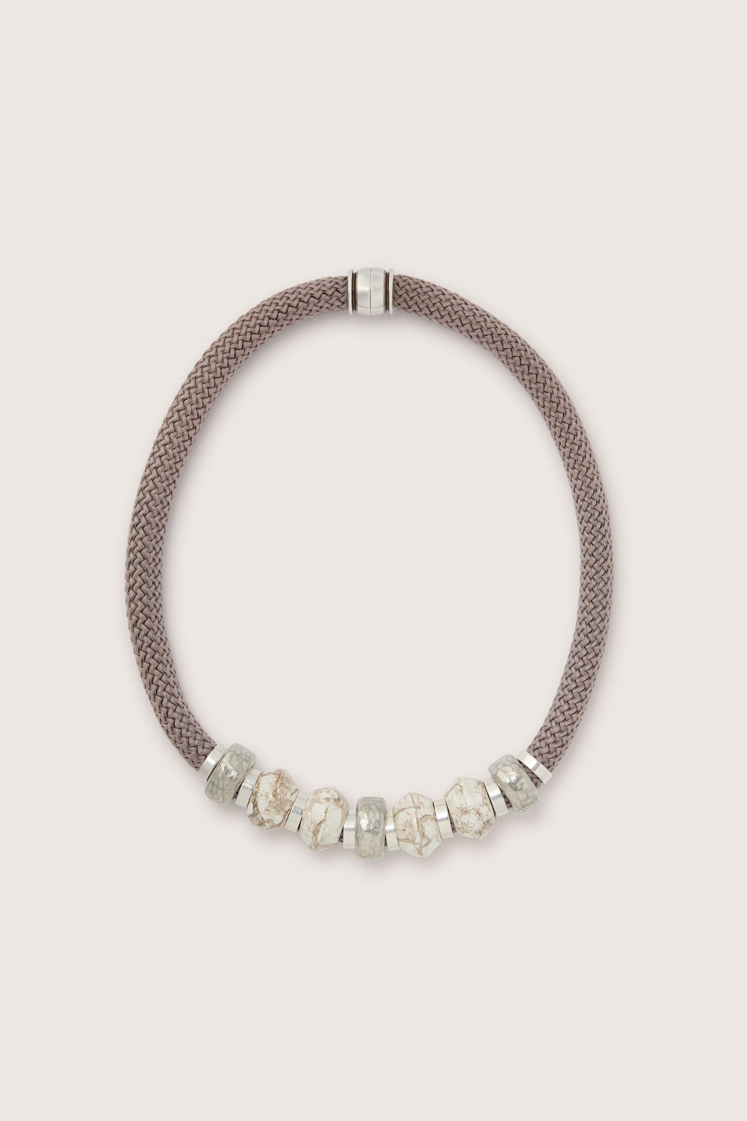 A brown braided necklace with a silver clasp, featuring seven silver and beige decorative beads. This Marble Bead Cord Necklace adds a sophisticated touch to any outfit.