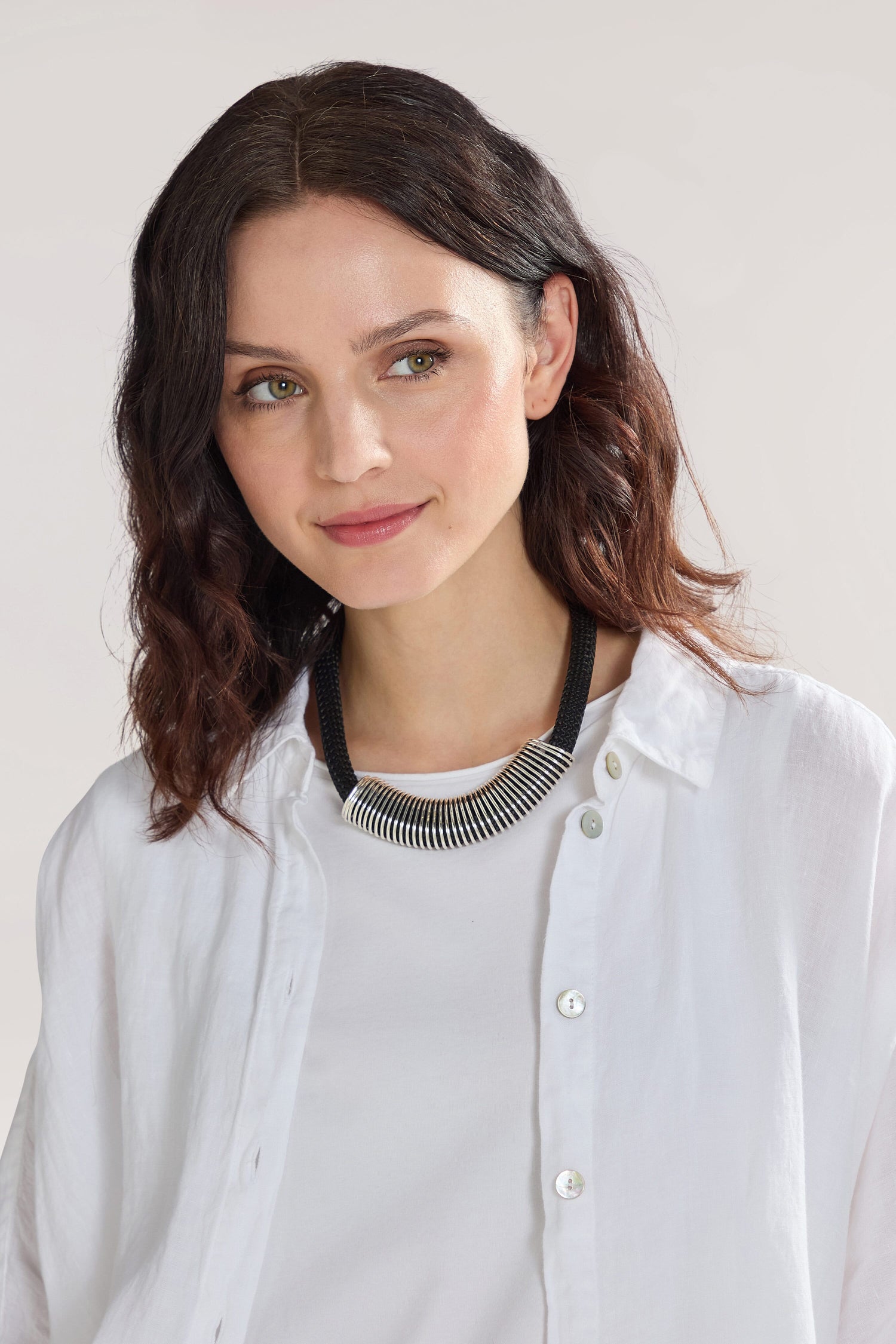 Woman with dark, wavy hair wearing a white shirt and a Spring Cord Necklace featuring a silver spring pendant, smiling slightly against a neutral background.