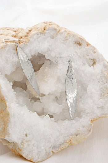 Two Hammered Silver Leaf Earrings are displayed on a large white crystal rock.