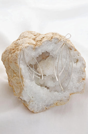 Arc Silver Earrings, with their luxurious, dangling leaf shape, are elegantly displayed on a white crystal rock.