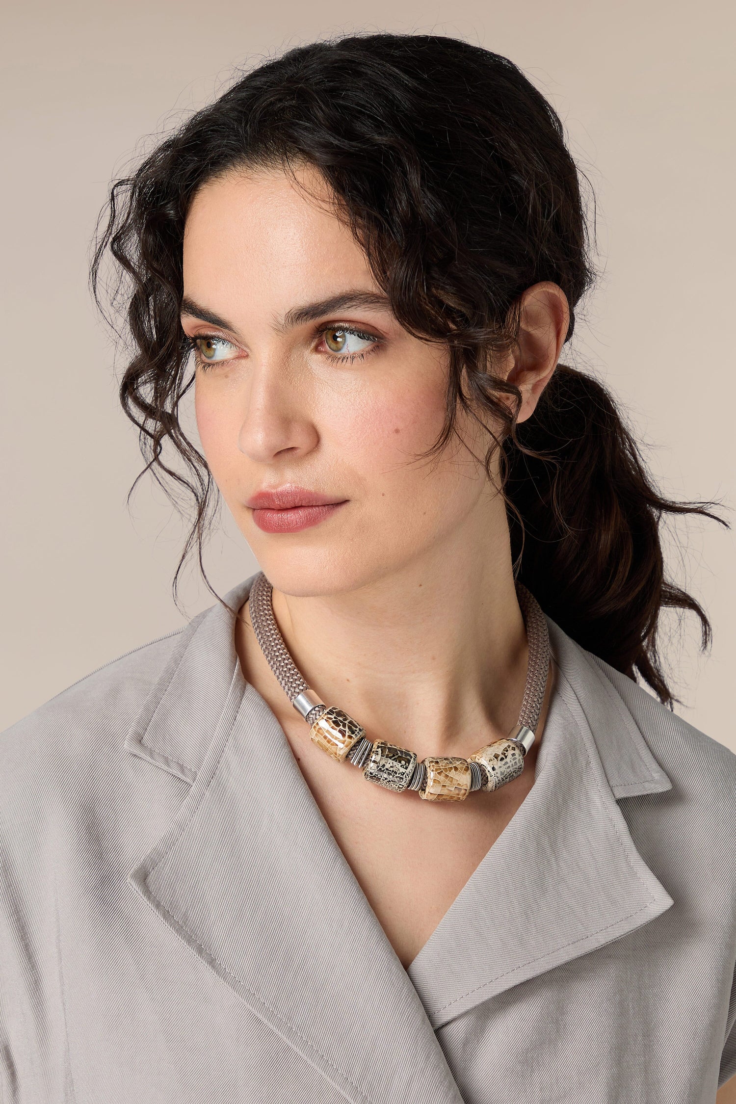 A woman wearing a Ceramic Bead Cord Necklace with ceramic beads and a grey blazer.