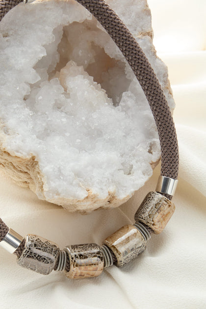 A handcrafted Ceramic Bead Cord Necklace rests on top of a rock.