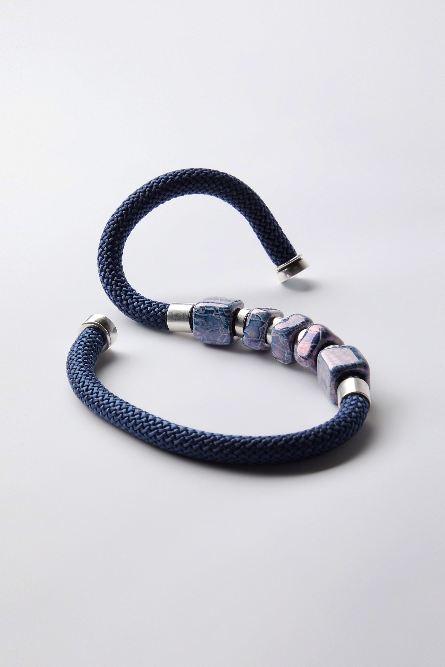 The Mosaic Cube Cord Necklace, featuring a braided blue cord, silver ends, and five marbled beads, displays artisanal craftsmanship on a white background.