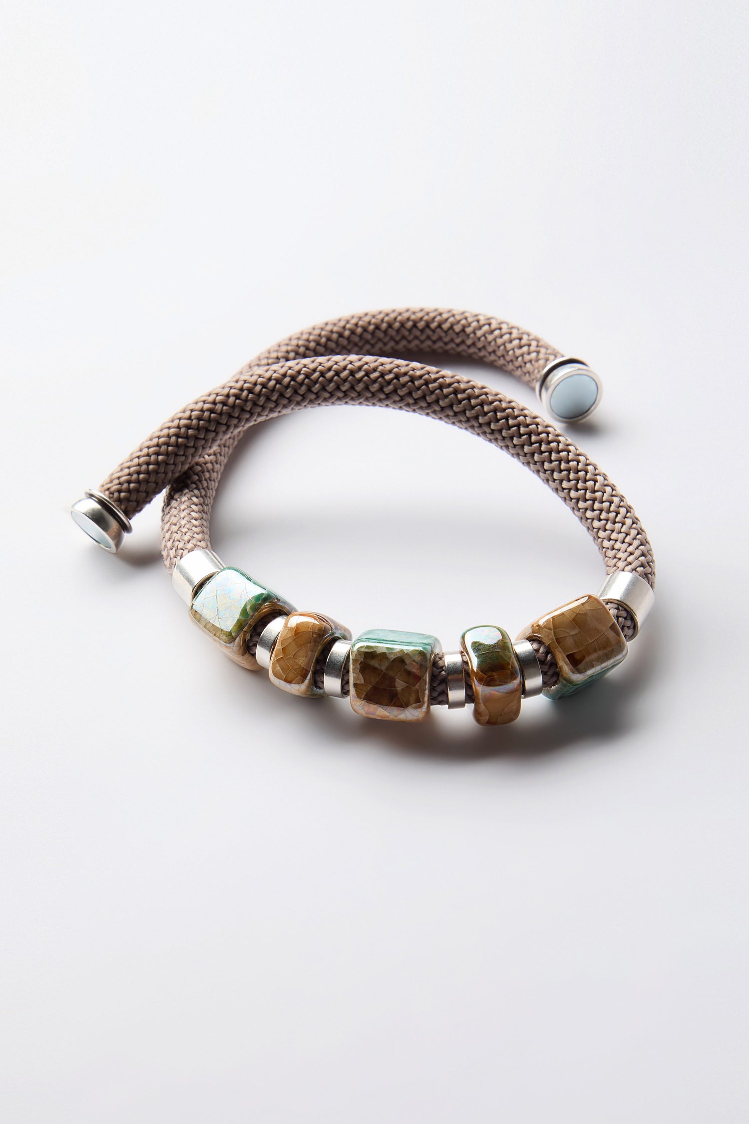 The Marble Cube Cord Necklace, featuring square multicolored stone beads and silver end caps, makes a contemporary statement as it coils on a white background.