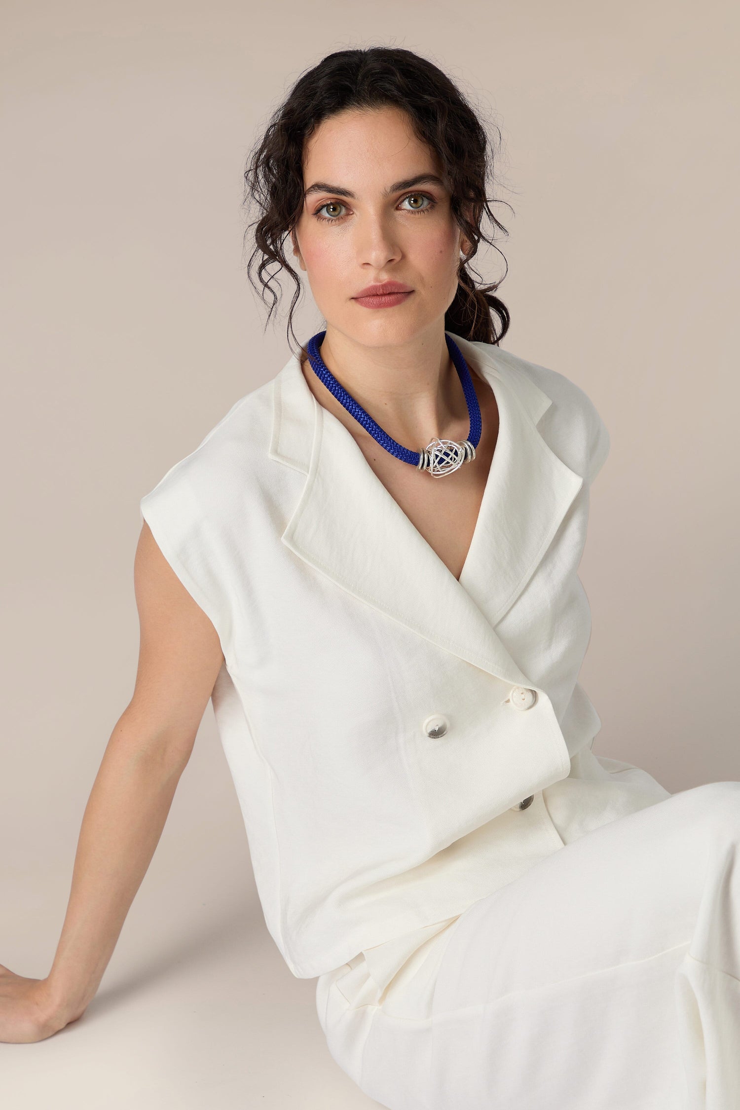 A woman in white sitting on the floor with a Mini Scribble Cord Necklace pendant.