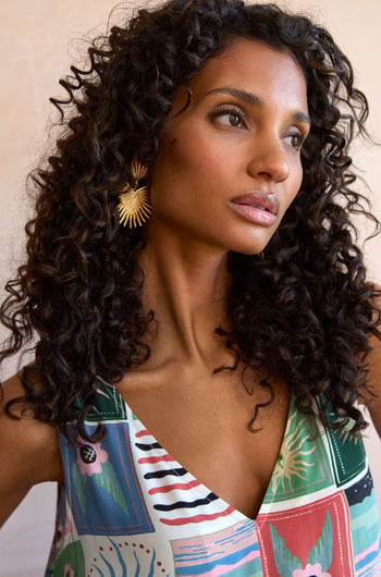 A woman with curly hair wears a patterned sleeveless top from EUNELECTRA-AW25 and Gold Plated Stargazer Earrings, looking slightly to the side.