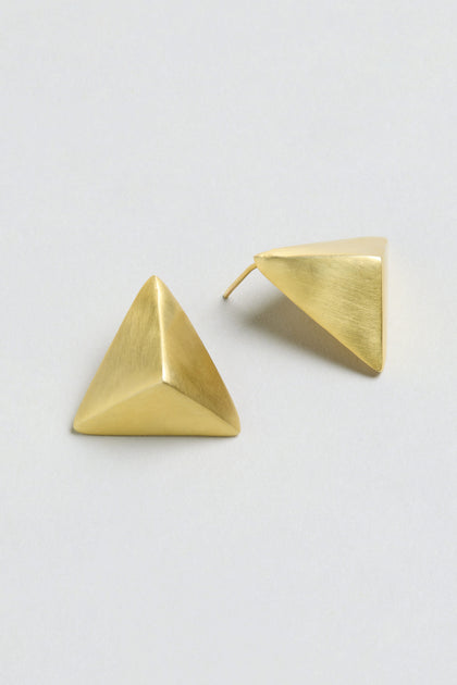 Folded Triangle Earrings crafted from recycled brass in a gold-tone geometric pyramid design, displayed on a light gray background; one earring lies flat while the other shows the back post.