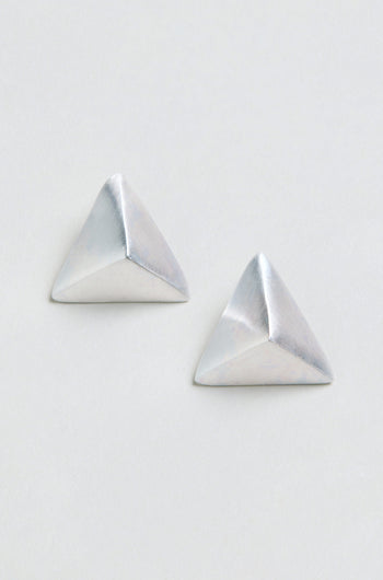 Two silver Folded Triangle Earrings, each featuring a pyramid-shaped geometric design, are displayed against a plain, off-white background.