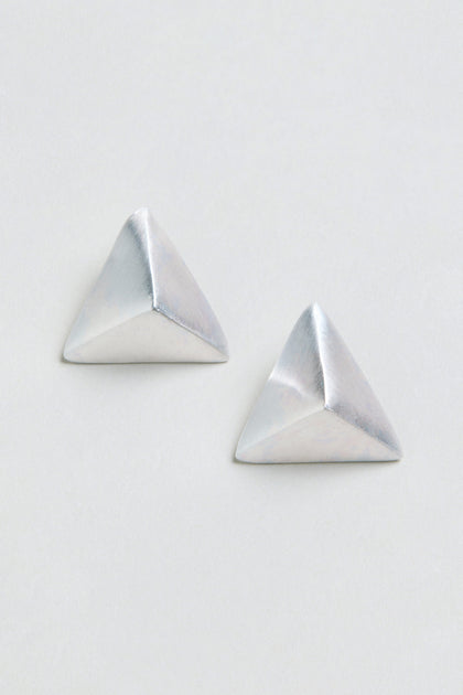 Two silver Folded Triangle Earrings, each featuring a pyramid-shaped geometric design, are displayed against a plain, off-white background.