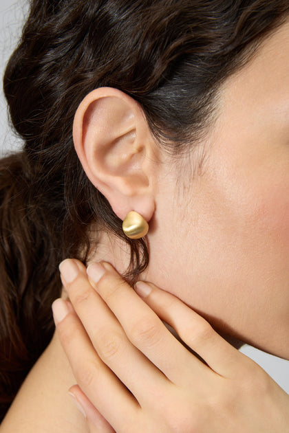 A close-up of a woman's ear wearing Gold Plated Mini Pebble Earrings, her hand gently resting on her neck.