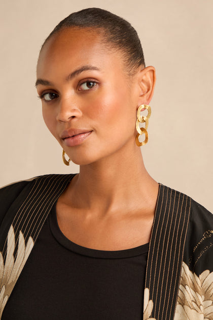 Woman with pulled-back hair wearing Gold Triple Hoop Earrings, a black top, and a patterned black jacket, posing against a neutral background.