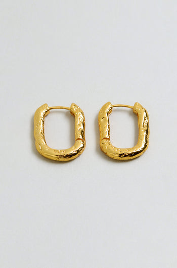 A pair of gold plated, rectangular hammered hoop earrings with a textured, uneven surface, displayed on a plain light background.