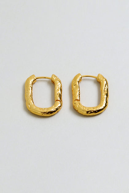 A pair of gold plated, rectangular hammered hoop earrings with a textured, uneven surface, displayed on a plain light background.