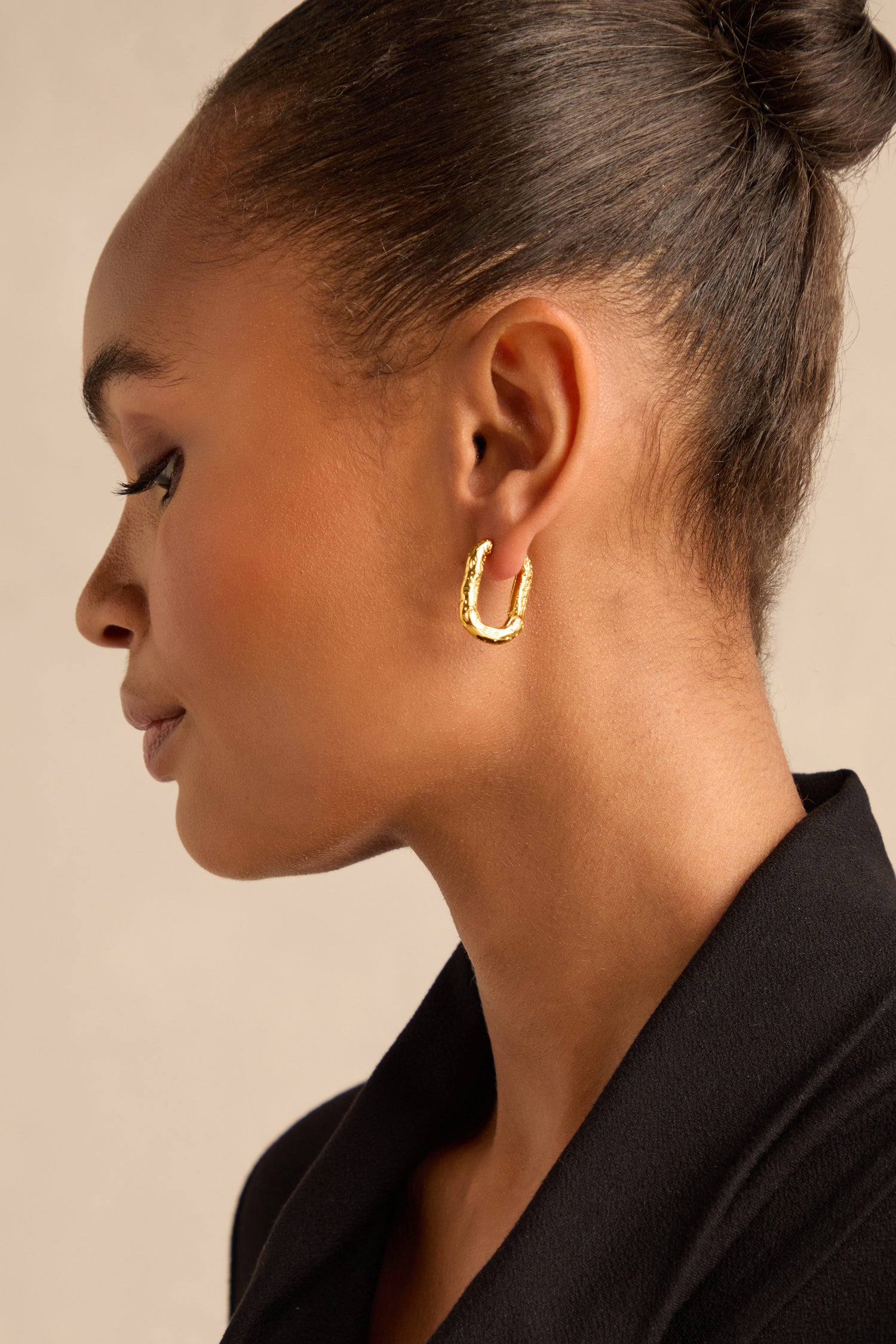 A woman with a neat bun, wearing a black blazer and the Hammered Hoop Earrings, is shown in profile against a neutral background.
