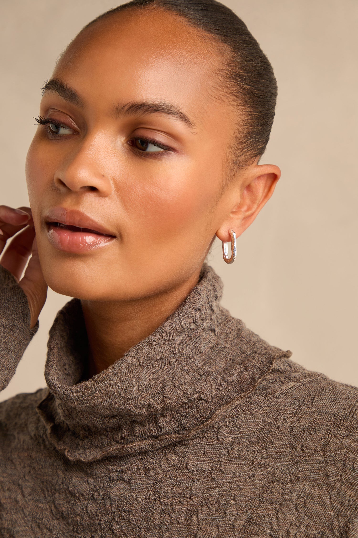 A woman with a neat bun wears the Hammered Hoop Earrings and a textured brown turtleneck sweater, gazing slightly to the side against a neutral background.