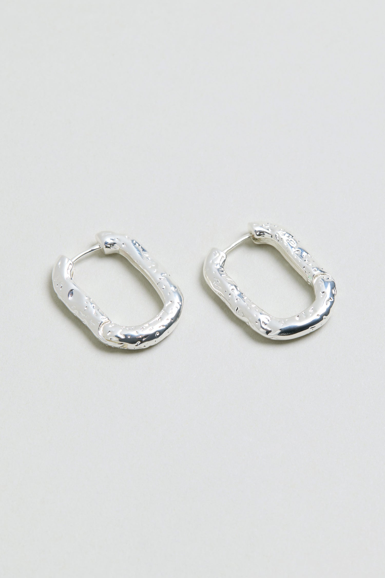 A pair of Hammered Hoop Earrings with a small, rectangular shape and textured hammered finish, displayed on a plain light gray surface.