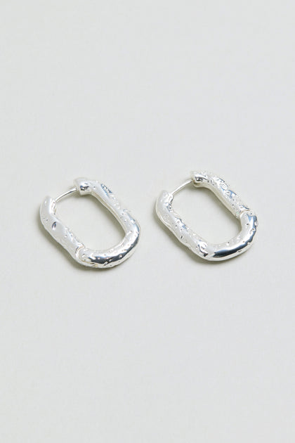 A pair of Hammered Hoop Earrings with a small, rectangular shape and textured hammered finish, displayed on a plain light gray surface.