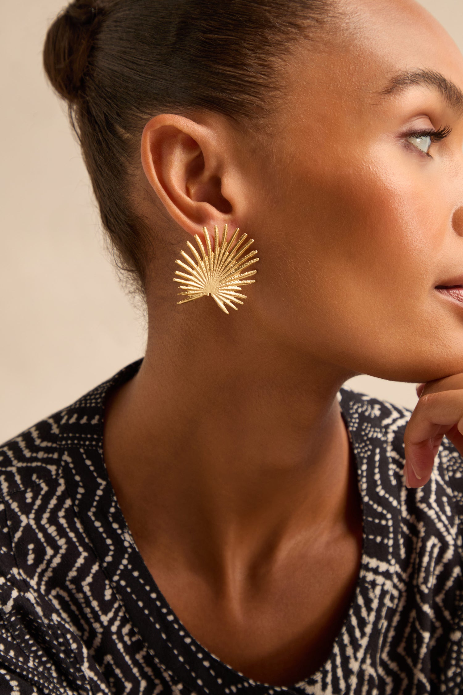 A person wearing a black and white patterned top is pictured in close-up from the side, showcasing the intricate design of the bold Sunburst Fan Earrings.