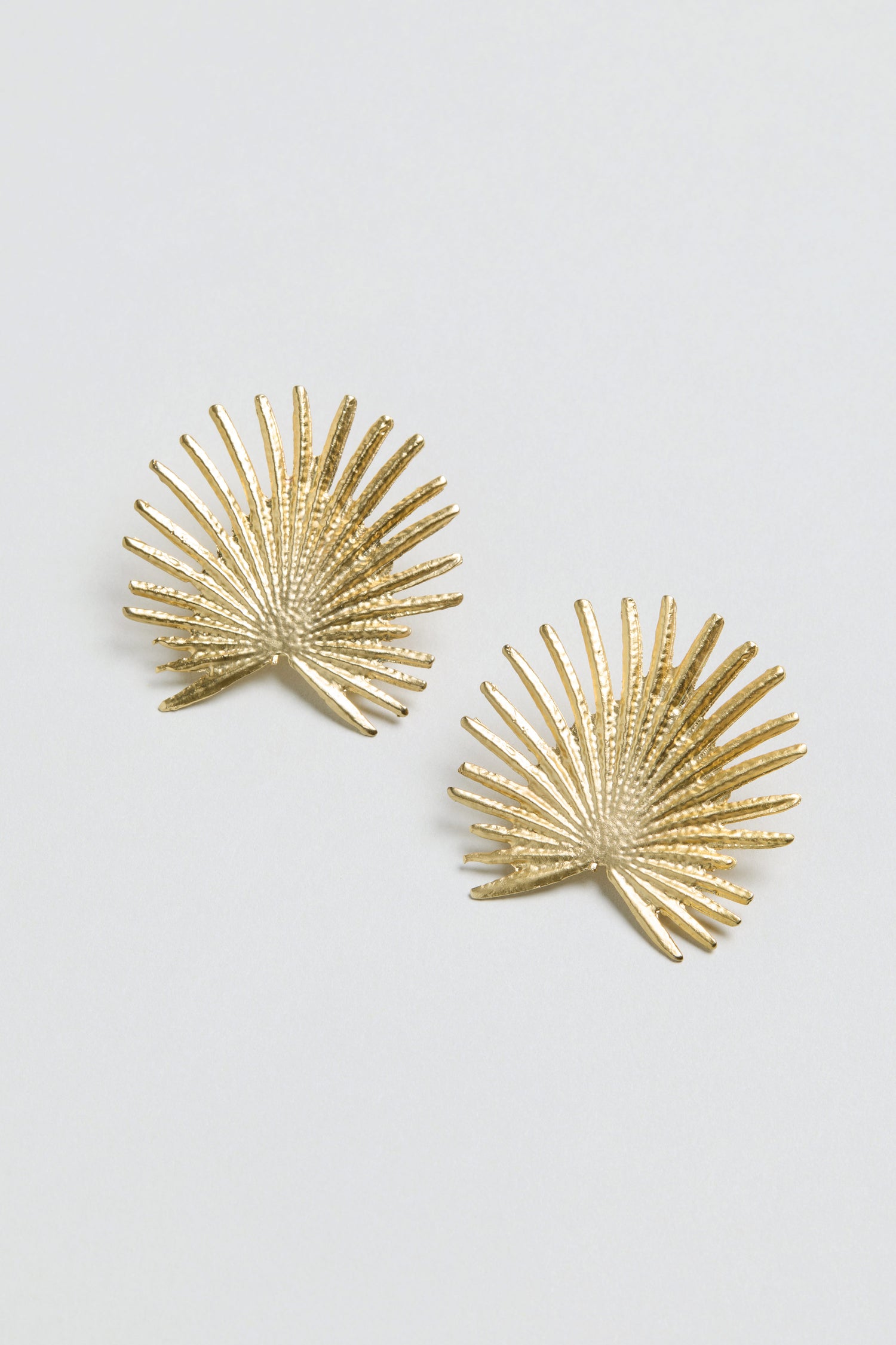 A pair of Sunburst Fan Earrings—gold plated statement studs inspired by palm leaves—displayed on a plain white background.