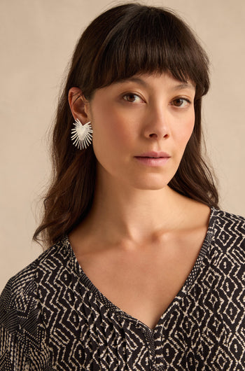 A woman with long dark hair and bangs wears a patterned black-and-white top and the Sunburst Fan Earrings, standing against a neutral background.