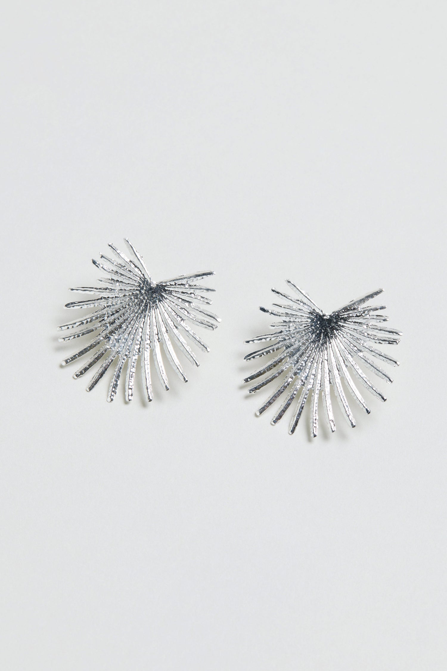 The Sunburst Fan Earrings are a silver pair featuring radiating textured spikes in a sunburst design, displayed on a plain white background.