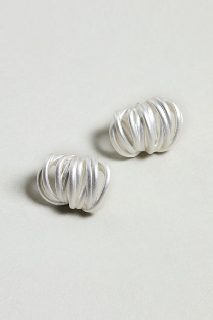 The Silver Vortex Earrings are modern silver loop earrings featuring a twisted design, shown on a plain light surface.