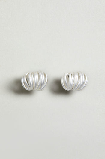 The Silver Vortex Earrings are sculptural, silver studs with a spiral shape, showcased against a simple light background.