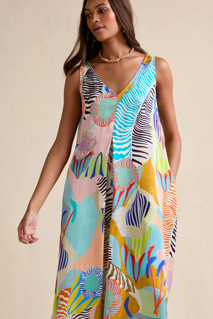 A woman models the Tropical Fantasy Sleeveless Dress, featuring a vibrant abstract pattern, against a neutral backdrop.
