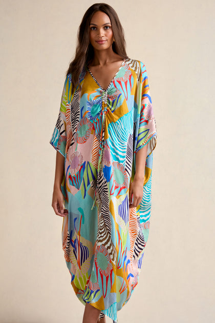 A woman wears a loose, colorful Tropical Fantasy Kaftan featuring a V-neck and short sleeves, standing against a plain background.