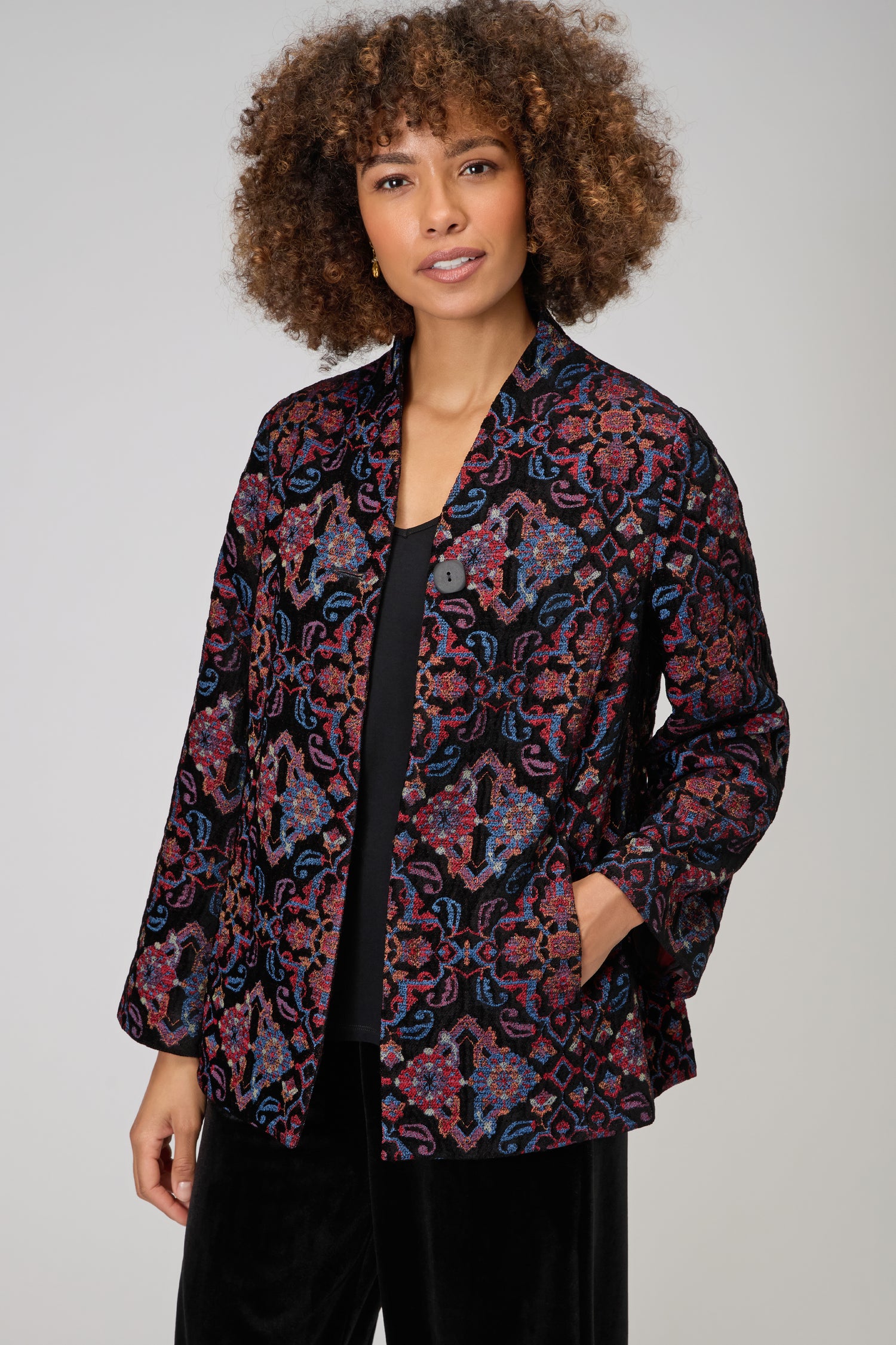 A woman poses against a plain background in the Baroque Chenille Jacket, layered over a black top, with one hand casually in her pocket.