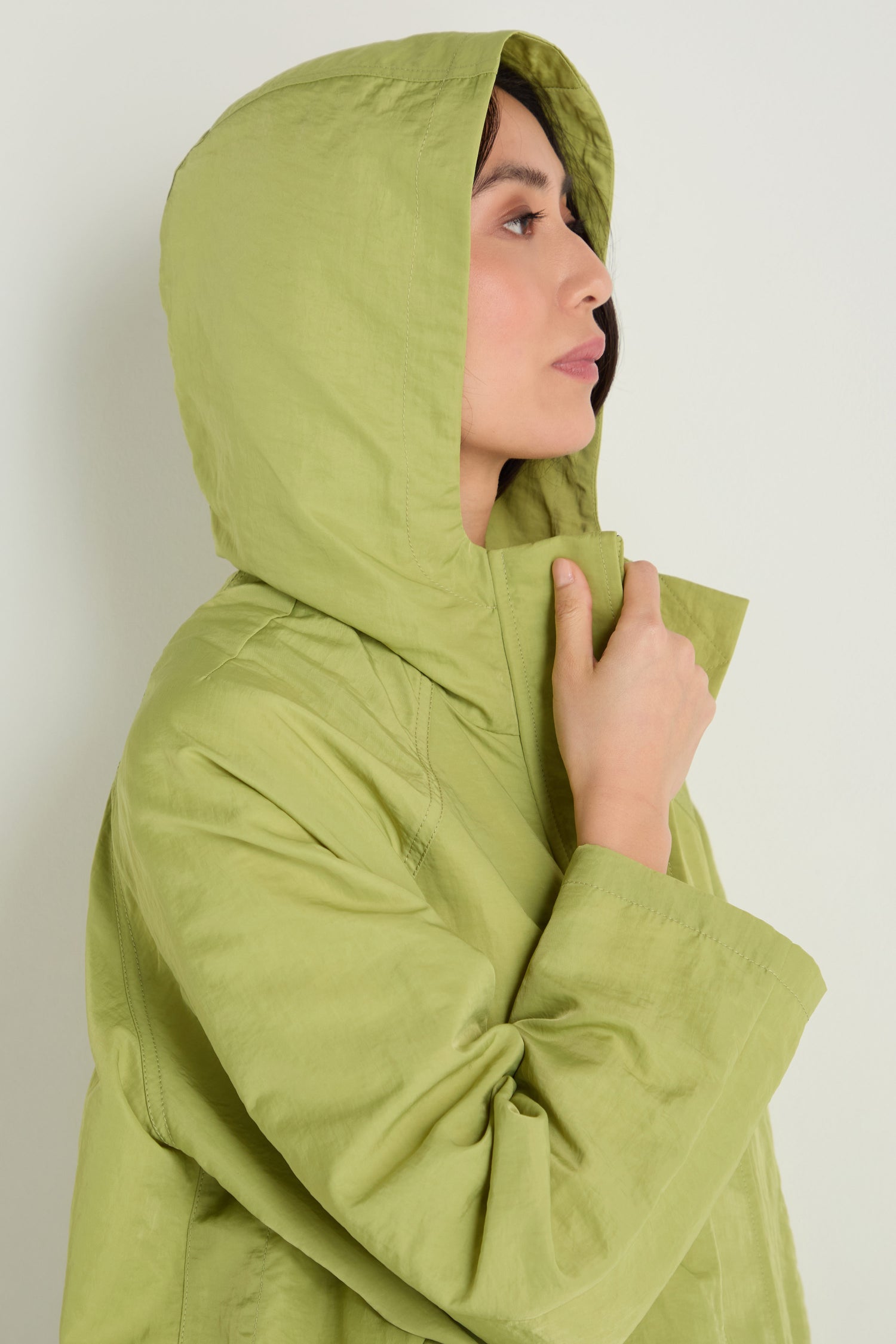 Wearing the Showerproof Boxy Rain Jacket in light green, a person holds the collar and looks to the side against a plain background.