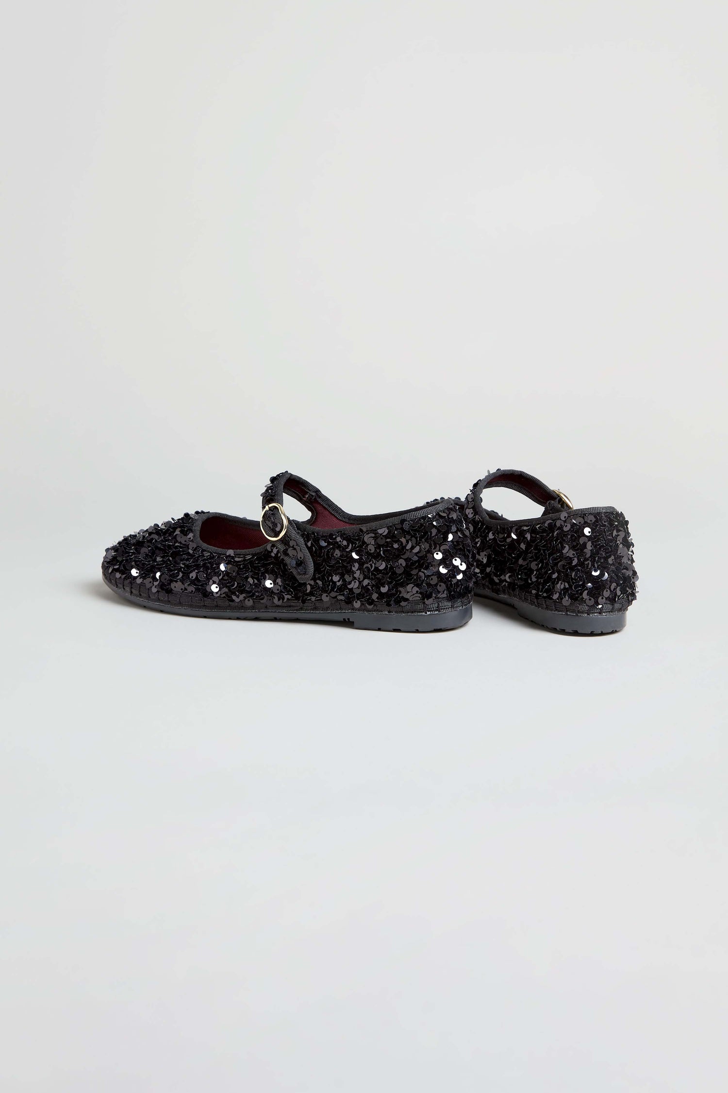 A pair of Sequin Mary Jane Shoes in black, handcrafted in Spain with classic buckle straps, shown against a light neutral backdrop.