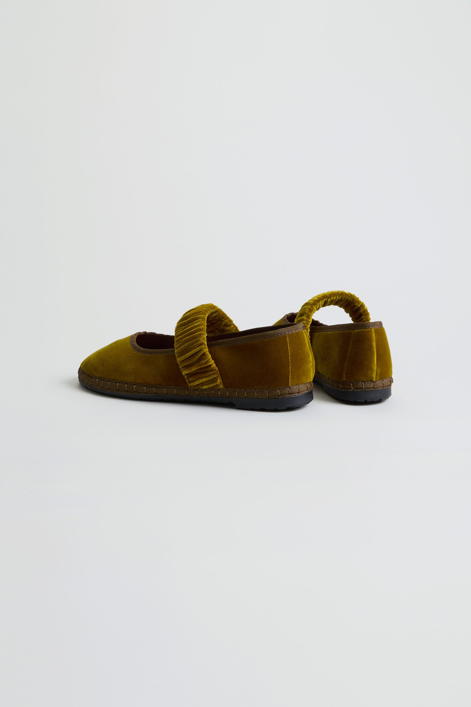 The Mafalda Ochre Velvet Shoes are a pair of Mary Jane-style shoes in mustard yellow, featuring ruched straps, handmade in Spain with black recycled rubber soles, shown against a plain white background.