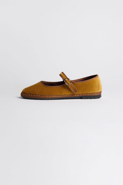 The Mustard Mary Jane Velvet Shoes feature a brown buckle strap and sole, displayed in profile on a white background, showcasing sustainable craftsmanship inspired by traditional Spanish shoemaking.