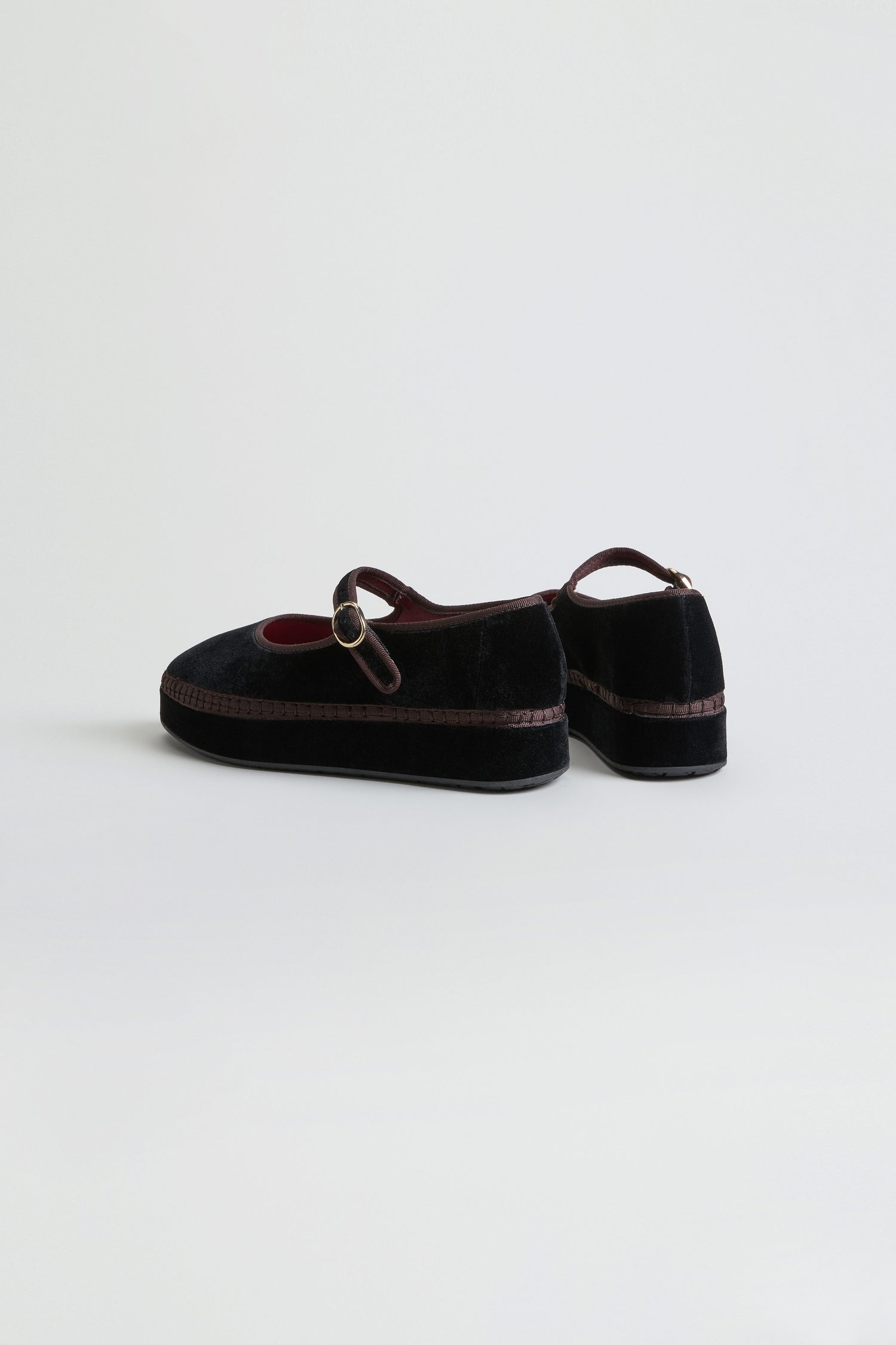 A pair of Black Velvet Platform Mary Jane Shoes with a strap and buckle, featuring a thin brown trim along the recycled sole, is displayed on a plain white background.