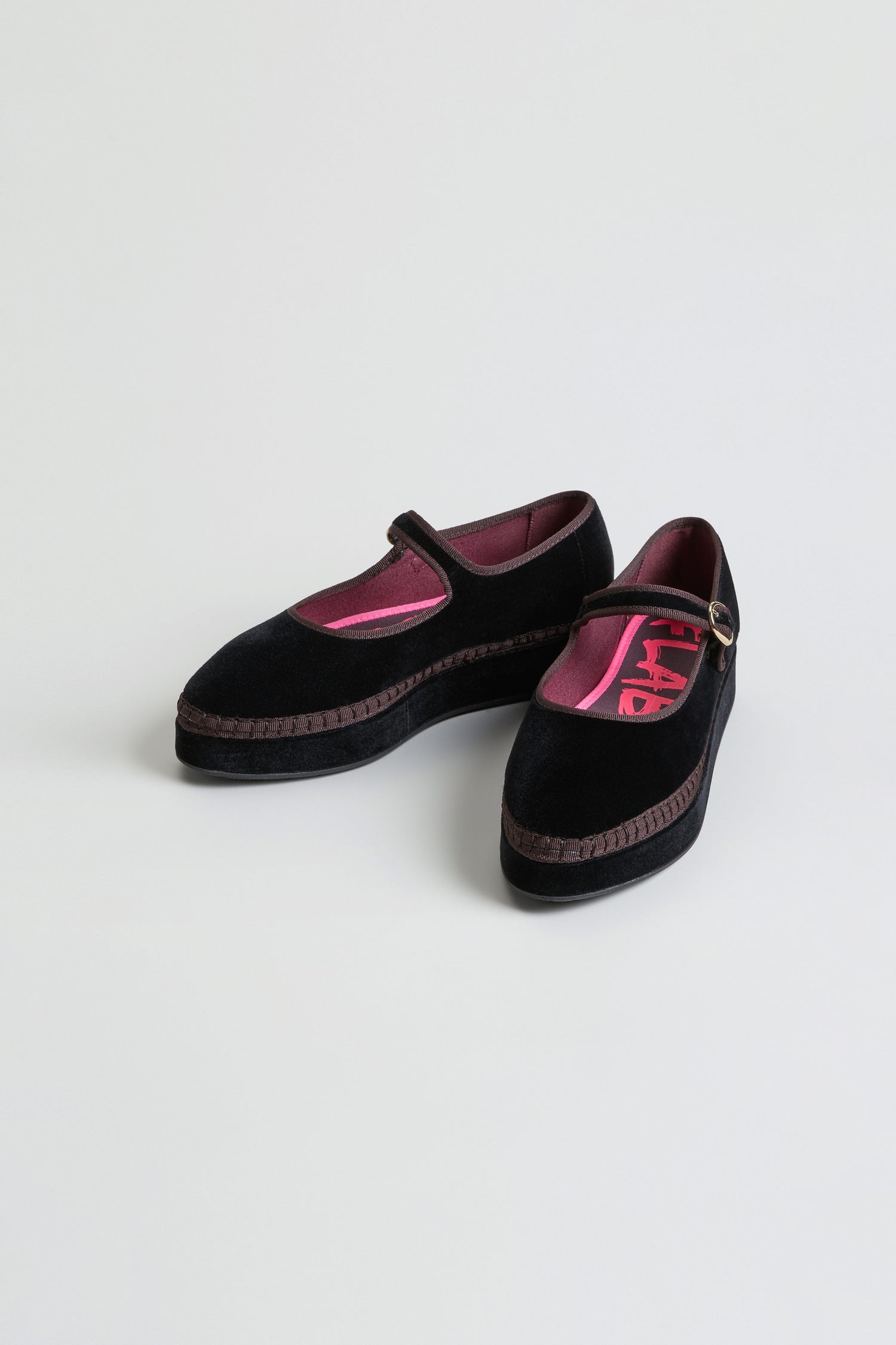 The Black Velvet Platform Mary Jane Shoes feature brown trim, a pink inner lining, and a buckle strap, and are displayed on a plain light background.
