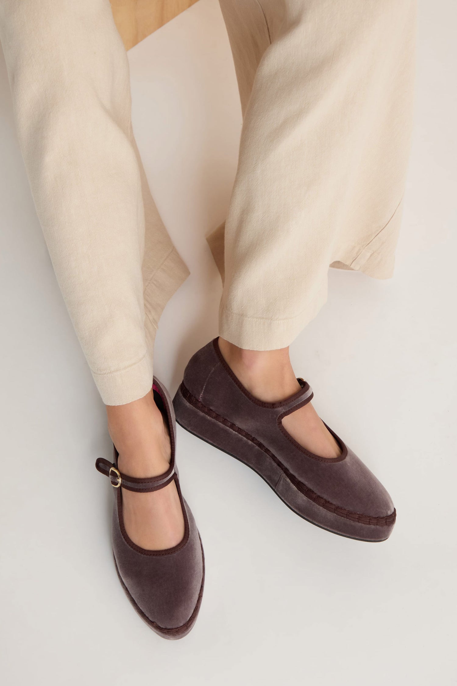 Person wearing beige pants and Taupe Velvet Platform Mary Jane Shoes with a buckle strap and soft cotton velvet upper, seated on a light surface.
