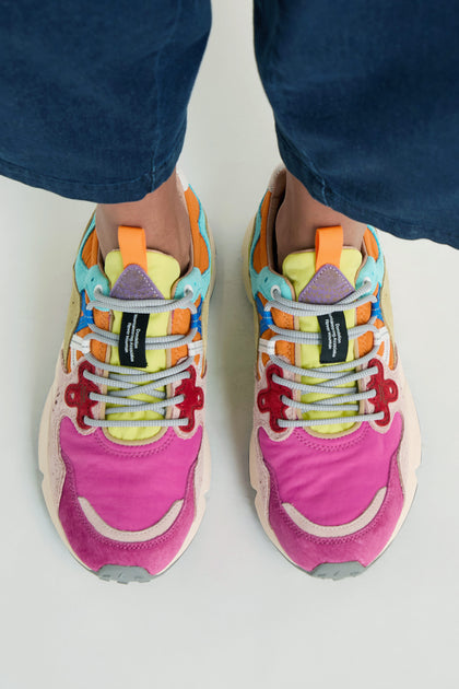 A person stands on a light surface wearing Fuchsia Yamano 3 Colour Pop Trainers. Photographed from above, the outdoor-inspired sneakers showcase their vibrant pink, yellow, blue, orange, and beige accents.
