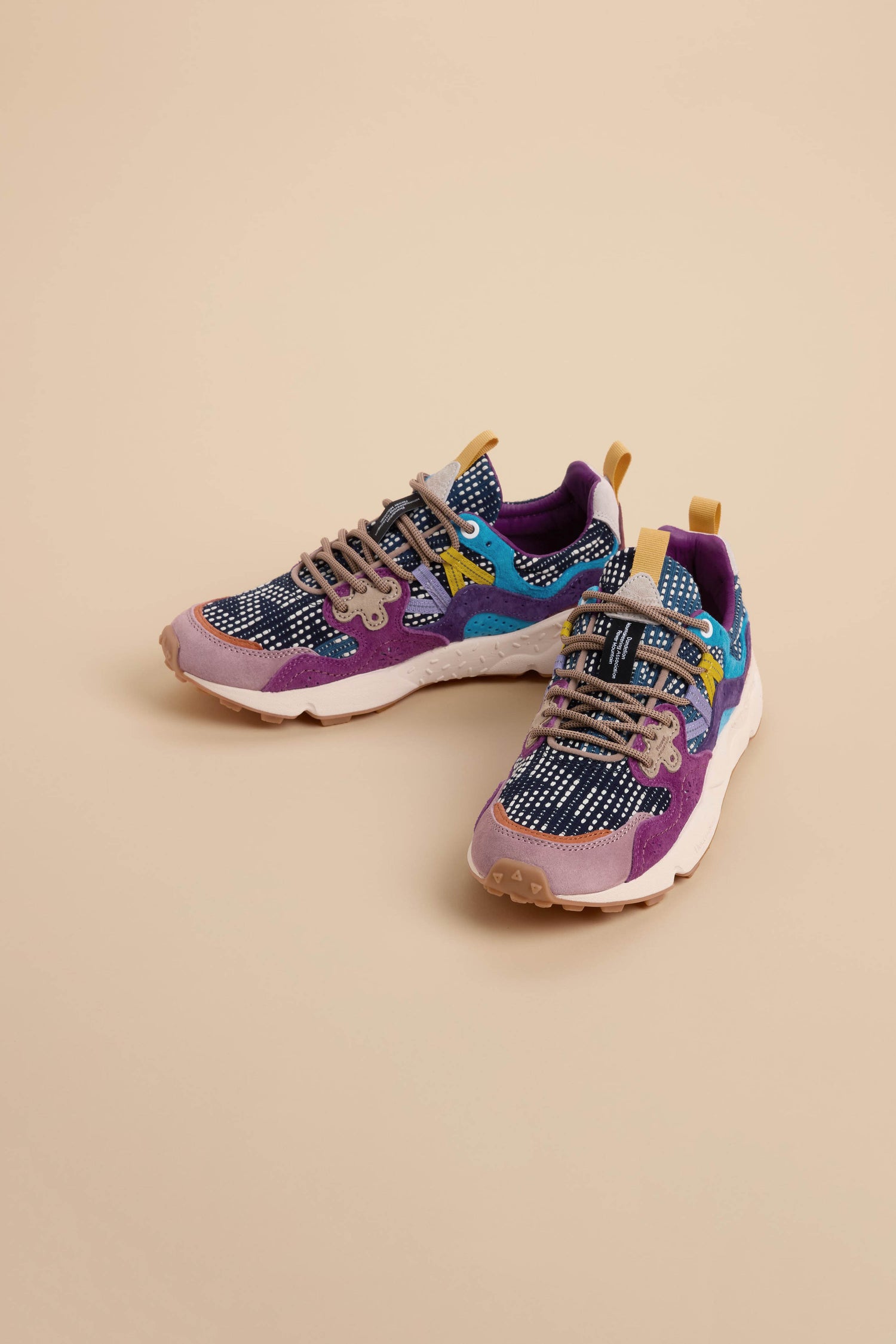 A pair of multicolored athletic sneakers with purple, blue, tan, and black accents on a beige background, drawing inspiration from the unique design of Yamano 3 Katsuo Sashi Trainers.