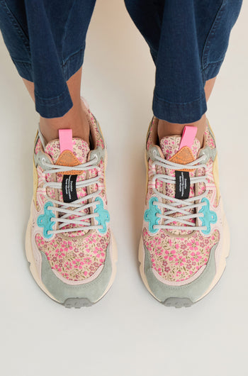 Person in dark blue pants standing on a light surface, wearing Yamano 3 Floral Trainers with floral patterns and light blue and pink accents inspired by Flower Mountain.
