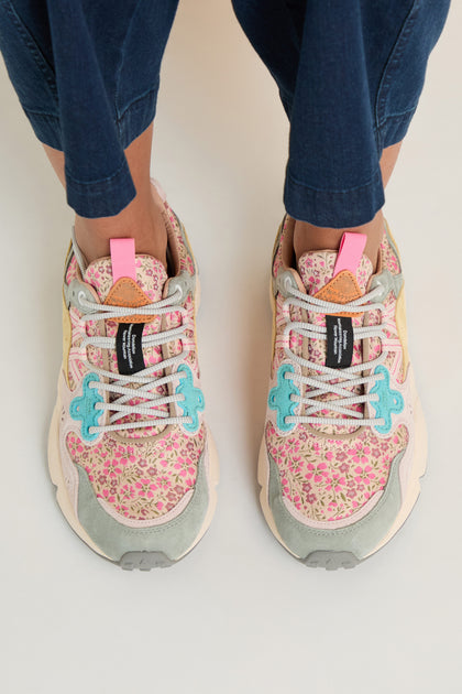 Person in dark blue pants standing on a light surface, wearing Yamano 3 Floral Trainers with floral patterns and light blue and pink accents inspired by Flower Mountain.