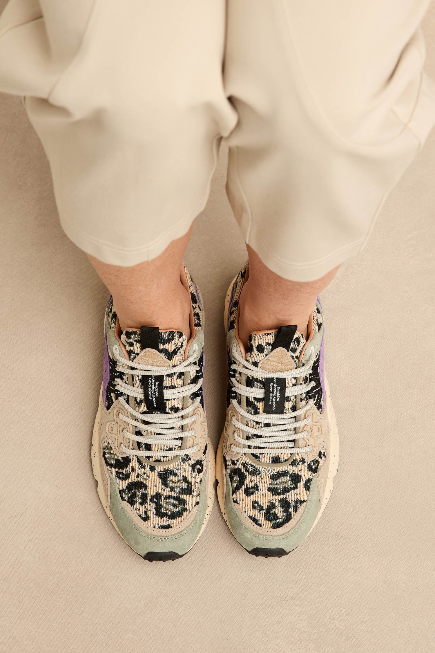 Person wearing beige pants and Yamano 3 Leopard Print Trainers with white laces and a stylish chunky sole, standing on a light-colored floor.