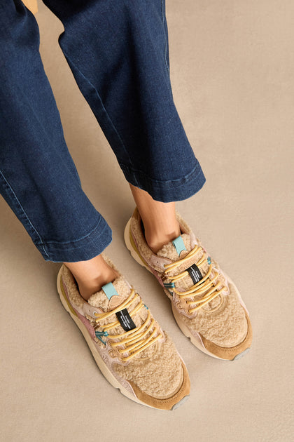 Person wearing blue pants and Yamano 3 Teddy Trainers with textured fabric, cork insole, and yellow laces, standing on a light tan surface.