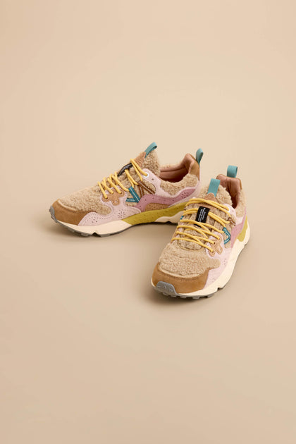 The Yamano 3 Teddy Trainers, featuring beige and tan uppers with yellow laces, blue and green accents, and a textured design, are displayed on a solid beige background.