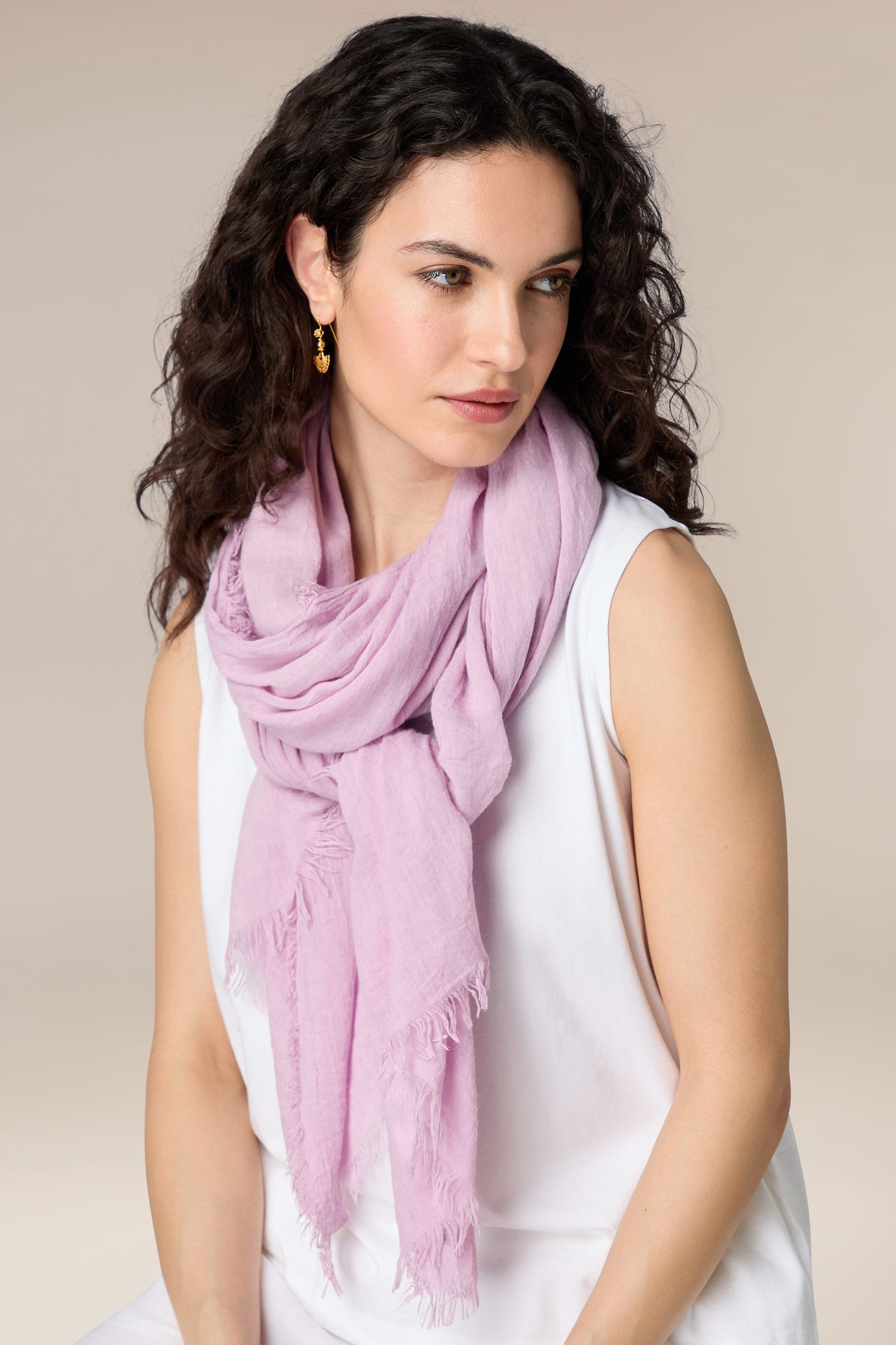 A woman wearing a white sleeveless top and a Celine Soft Fringe Scarf in light pink, a must-have accessory offering versatile styling options, looking to the side.