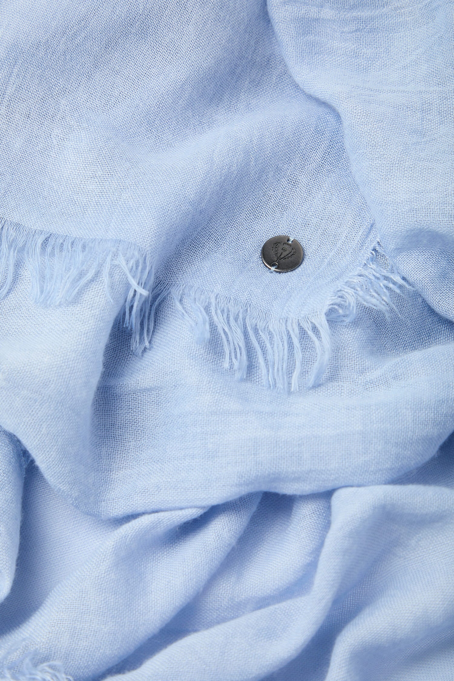 Close-up of a frayed Soft Fringe Scarf with a metallic button.