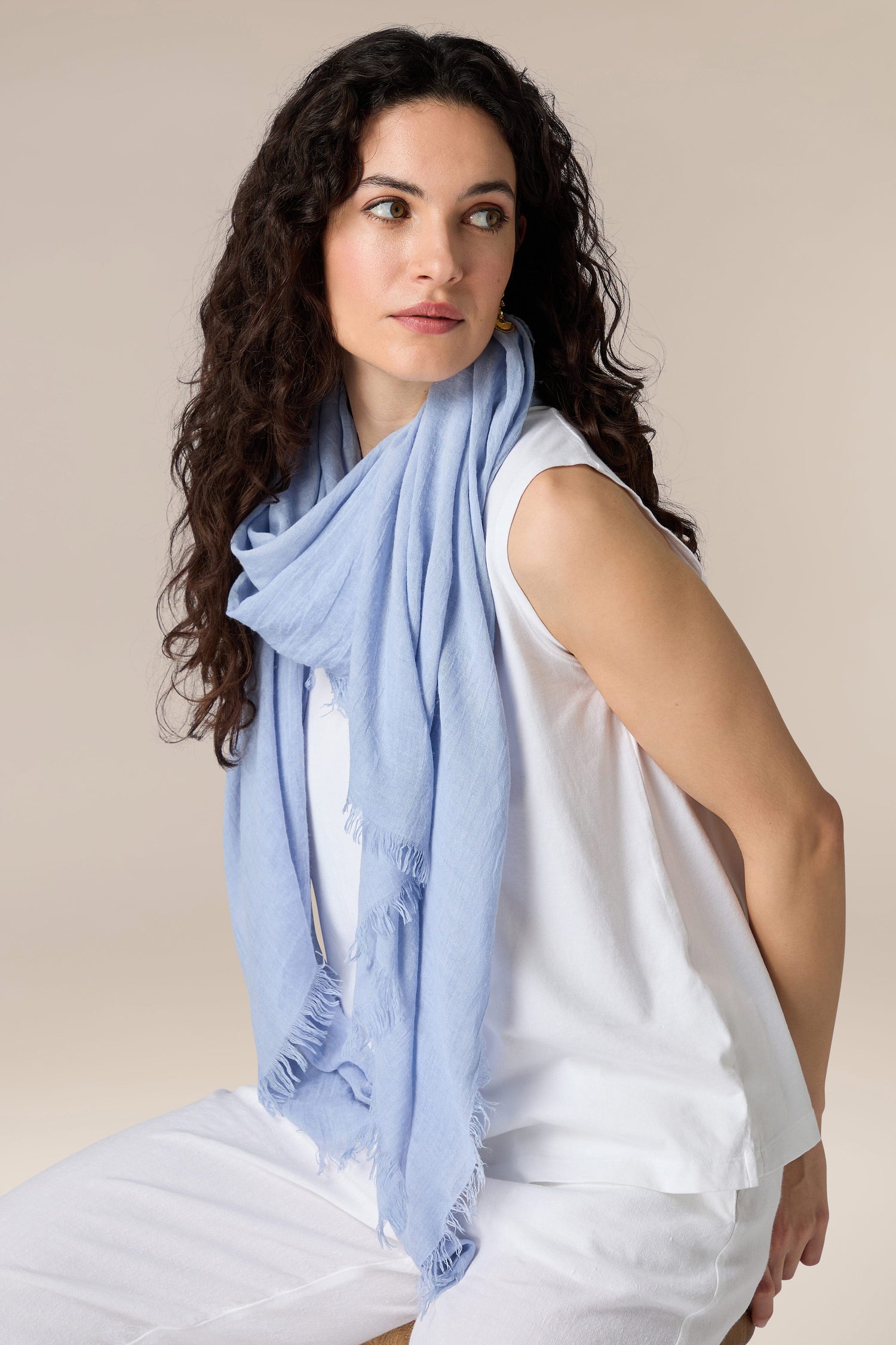 Woman with curly hair wearing a white blouse and a Soft Fringe Scarf with versatile styling options, looking to the side.